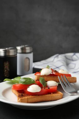 Mozarella peynirli, domatesli ve fesleğenli lezzetli sandviçler koyu renkli masada, yakın plan.