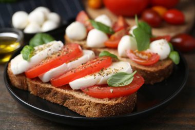 Peynirli, domatesli, fesleğenli ve baharatlı lezzetli sandviçler ahşap masada, yakın plan.