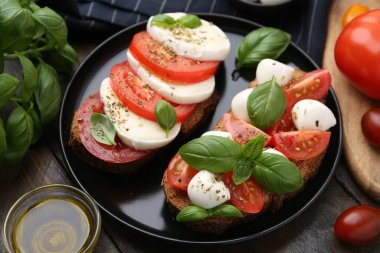 Peynirli, domatesli, fesleğenli ve baharatlı lezzetli sandviçler ahşap masada, yakın plan.