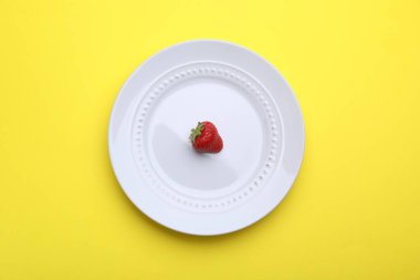 Sarı arka planda taze çilekli tabak, üst manzara.