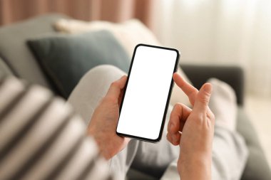 Evdeki koltukta modern akıllı telefon kullanan bir kadın.