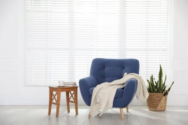 Rahat mavi koltuk, battaniye, yan masa ve ev bitkisi Beyaz duvar içinde, metin için yer