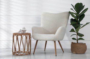 Rahat koltuk, yan masa ve beyaz duvarın yanındaki bitki örtüsü.