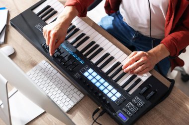 İçerideki ahşap masada MIDI klavyesiyle çalışan bir adam.