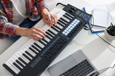 Beyaz masada MIDI klavyesiyle çalışan bir adam.,