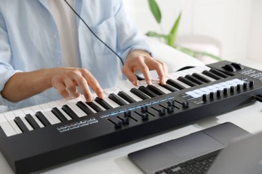 Beyaz masada MIDI klavyesiyle çalışan adam, yakın plan.