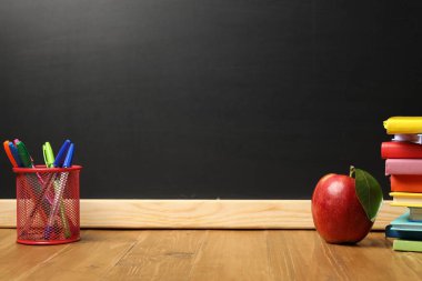 Tahtanın yanındaki ahşap masada farklı kırtasiye ve kırmızı elma, metin için yer