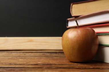 Tahtanın yanındaki ahşap masada farklı kitaplar ve elmalar, yakın plan. Metin için boşluk