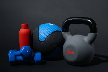 Siyah arka planda ilaç topu, halterler, su şişesi ve su şişesi.