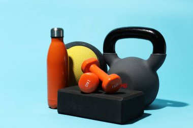 İlaç topu, kettlebell, su şişesi, köpük bloğu ve açık mavi arka plandaki dambıllar.