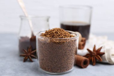 Granüle edilmiş hazır kahve ölçü kabı ve baharatlar gri masada, yakın plan.