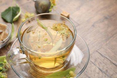 Fincanda taze ıhlamur çayı, şeker küpleri ve tahta masada çiçekler, yakın plan. Metin için boşluk