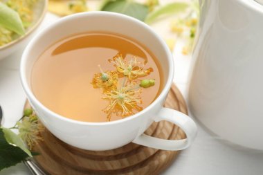 Fincanda taze ıhlamur çayı ve beyaz ahşap masada çiçekler, yakın plan.