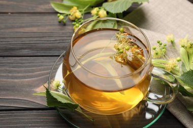 Fincanda taze ıhlamur çayı ve koyu ahşap masada çiçekler, yakın plan.