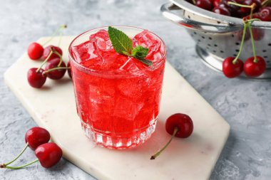 Buzlu vişneli gazoz, böğürtlen ve bardakta nane şekeri. Gri desenli masa, yakın plan.