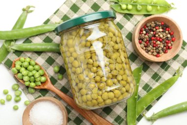 Kavanozda bezelye turşusu ve beyaz masada malzemeler.