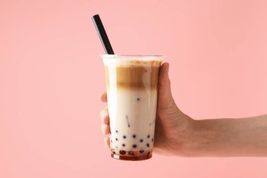 Pembe arka planda lezzetli sütlü çay içen kadın, yakın plan.