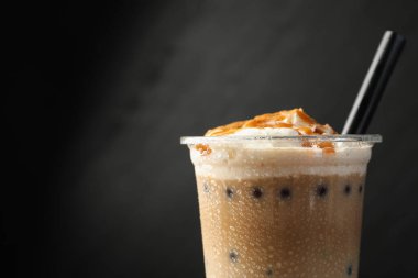 Siyah arka planda plastik bardakta lezzetli sütlü çay, yakın plan. Metin için boşluk