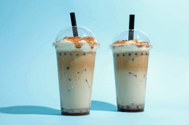 Açık mavi zemin üzerinde plastik bardaklarda lezzetli süt köpüğü çayı