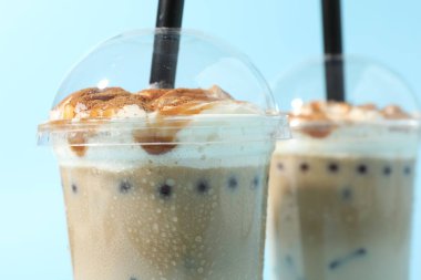 Açık mavi arkaplanda plastik bardaklarda lezzetli sütlü çay, yakın plan.