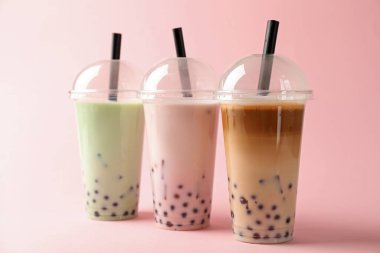 Pembe arka planda plastik bardakta lezzetli sütlü çay.