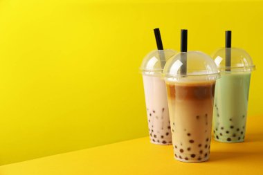 Sarı arka planda plastik bardakta lezzetli süt köpüğü çayı.