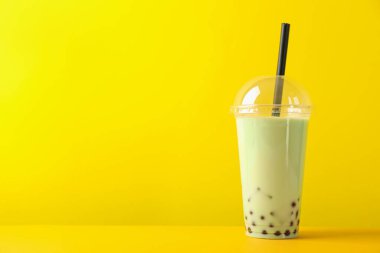 Sarı arka planda plastik bardakta lezzetli sütlü çay. Metin için boşluk