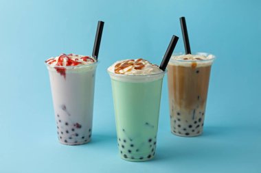 Açık mavi zemin üzerinde plastik bardaklarda lezzetli süt köpüğü çayı