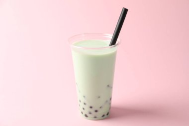 Pembe arka planda plastik bardakta lezzetli sütlü çay.