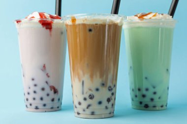 Açık mavi zemin üzerinde plastik bardaklarda lezzetli süt köpüğü çayı