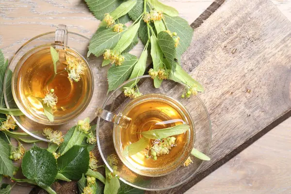 Fincanlarda nefis ıhlamur çayı, ahşap masada yapraklar ve çiçekler.