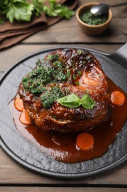 Biftek ve soslu geleneksel ossobuko tabağı ahşap masada servis edilir.