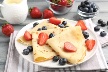 Gri ahşap masada meyveli ve kremalı leziz krepler, yakın plan.