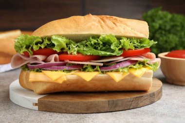 Gri desenli masada jambonlu, peynirli ve sebzeli baget sandviç, bulanık kahverengi arka plan, yakın plan.