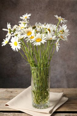 Tahta masadaki vazoda, kahverengi desenli arka planda birçok güzel papatya çiçeği, yakın plan.