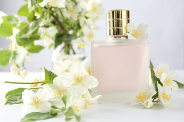 Beyaz masada bir şişe parfüm ve yasemin çiçeği, yakın plan.