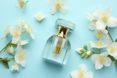 Bir şişe parfüm ve açık mavi arka planda güzel yasemin çiçekleri.