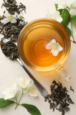 Cam bardakta Aromatik yasemin çayı, beyaz masada çiçekler ve yapraklar, düz uzanmış
