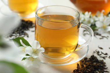 Cam bardakta Aromatik yasemin çayı, beyaz masada çiçekler ve kuru yapraklar, yakın çekim