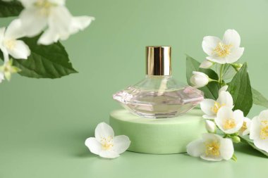 Yeşil arka planda bir şişe parfüm ve yasemin çiçeği, yakın plan.