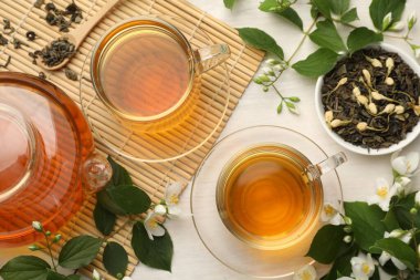 Lezzetli yasemin çayı fincanda, çaydanlıkta, kuru yapraklarda ve çiçeklerde beyaz ahşap masada, düz yerde.