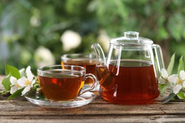 Lezzetli yasemin çayı fincanda, çaydanlık ve çiçekler ahşap masada, yakın plan.