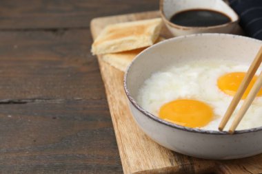 Geleneksel Asya kahvaltısı kasede yarı haşlanmış yumurta, soya sosu, ekmek ve çubuklar ahşap masada, yakın plan. Metin için boşluk