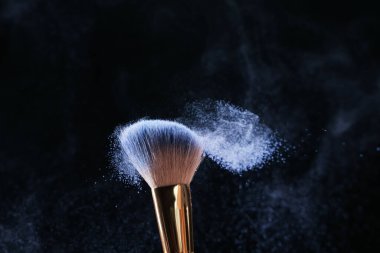 Siyah arkaplanda kozmetik ürünle makyaj fırçası, yakın plan