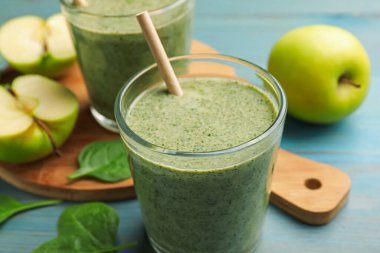 Lezzetli ıspanaklı smoothie ve açık mavi ahşap masa üzerindeki malzemeler, yakın plan.