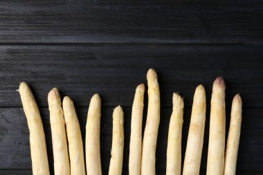 Çiğ beyaz kuşkonmaz mızrakları siyah ahşap masada, düz yerde. Metin için boşluk