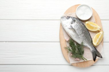 Beyaz ahşap masa üzerinde baharatlı taze çiğ dourade balığı, üst manzara ve yazı için yer. Deniz ürünleri lezzetleri.