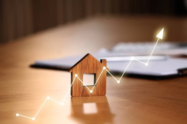 Gayrimenkul değerini arttır. Ev modeli ve belgeler masada. Artan fiyat okla temsil ediliyor