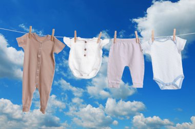 Mavi gökyüzüne karşı çamaşır ipinde kurumuş farklı bebek kıyafetleri.