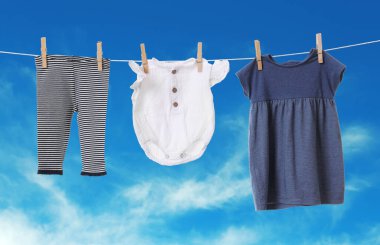 Mavi gökyüzüne karşı çamaşır ipinde kurumuş farklı bebek kıyafetleri.